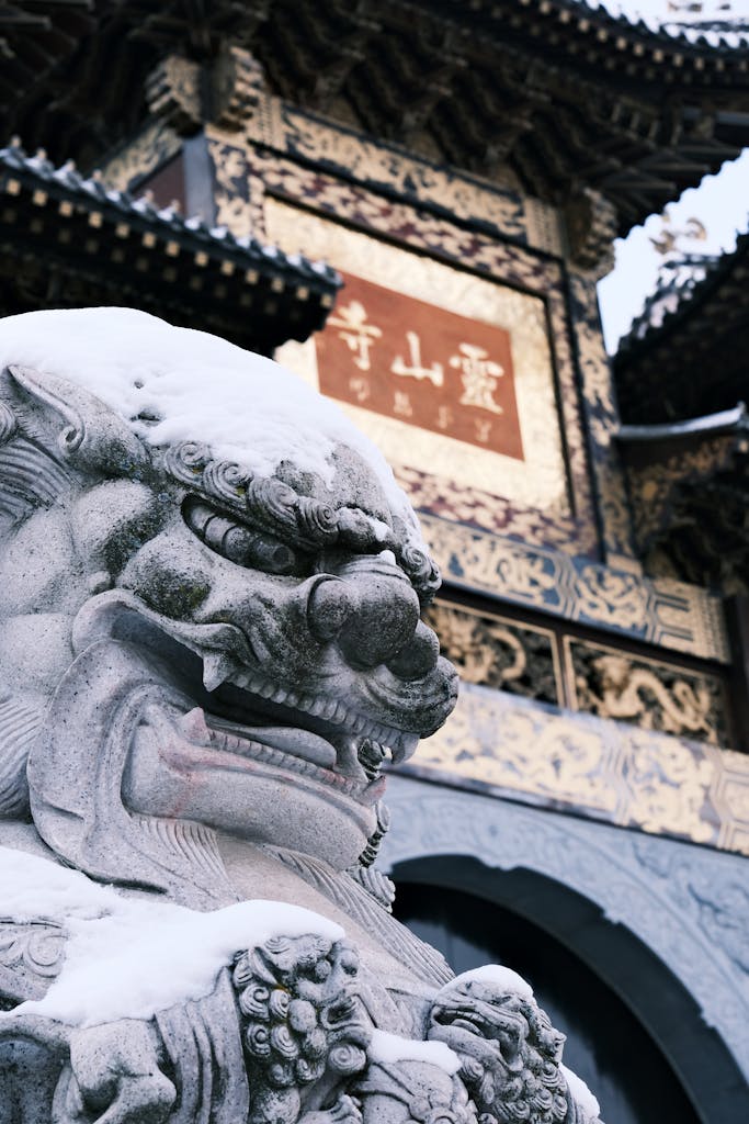 Close-up of a snow-covered stone lion statue in front of a traditional Chinese temple.