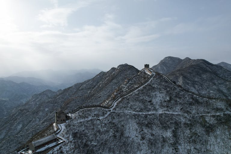 Stunning aerial view of the Great Wall of China covered in snow against a blue sky in winter.